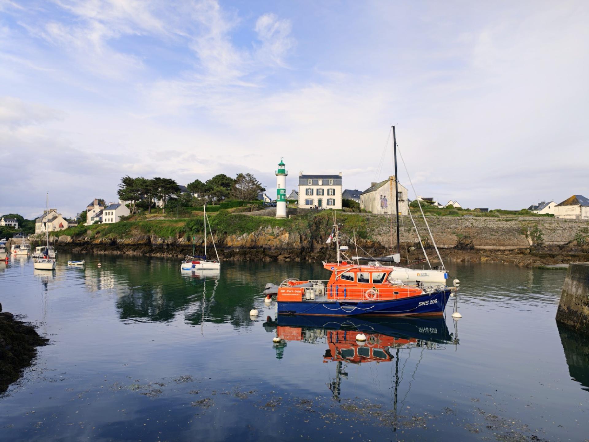 Des bateaux dans un port avec un phare vert en hauteur