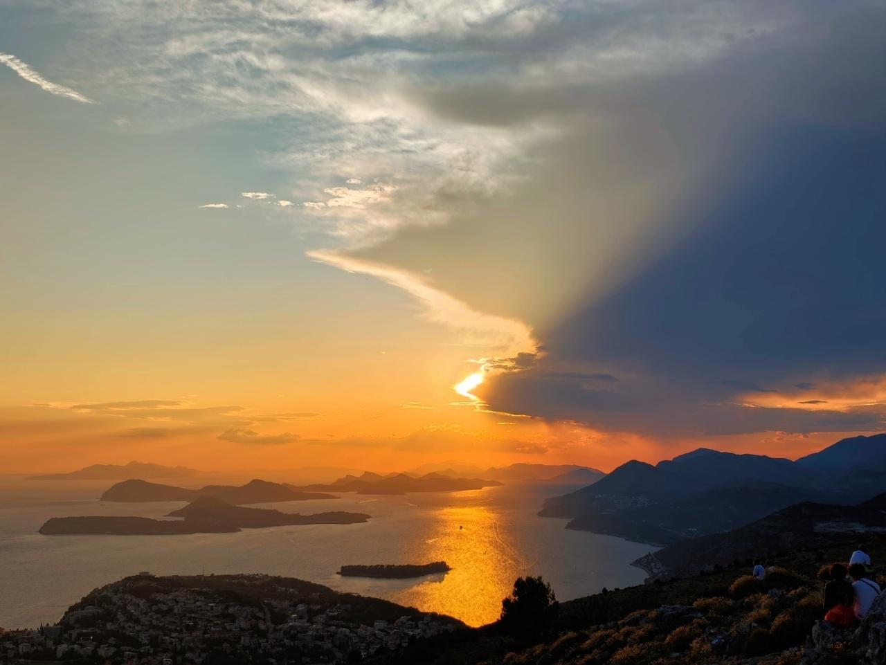 coucher de soleil sur l'Adriatique avec des îles et sommets à l'horizon, un nuage commence à cacher le soleil